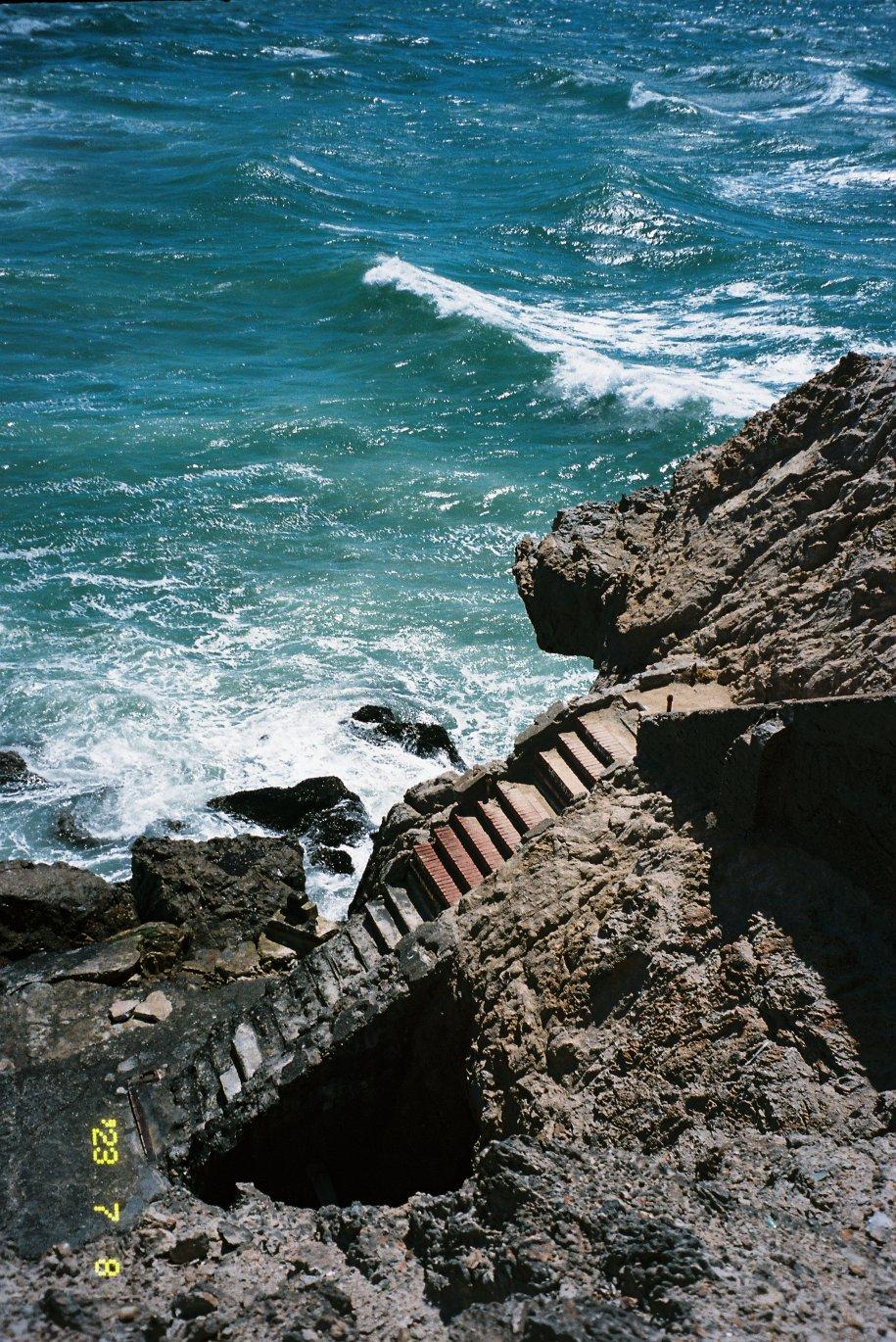 a worn concrete staircase carved into the rocky cliffside of an ocean