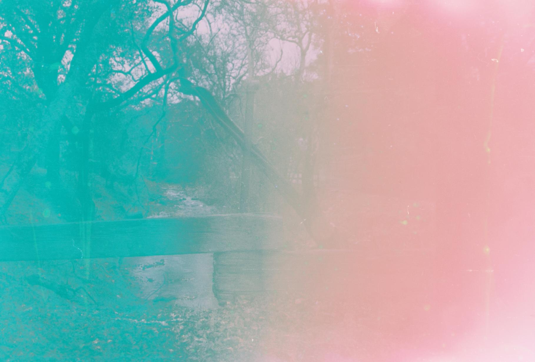 a small bridge overlooking a small creek with trees. half of the photo is missing due to film burn