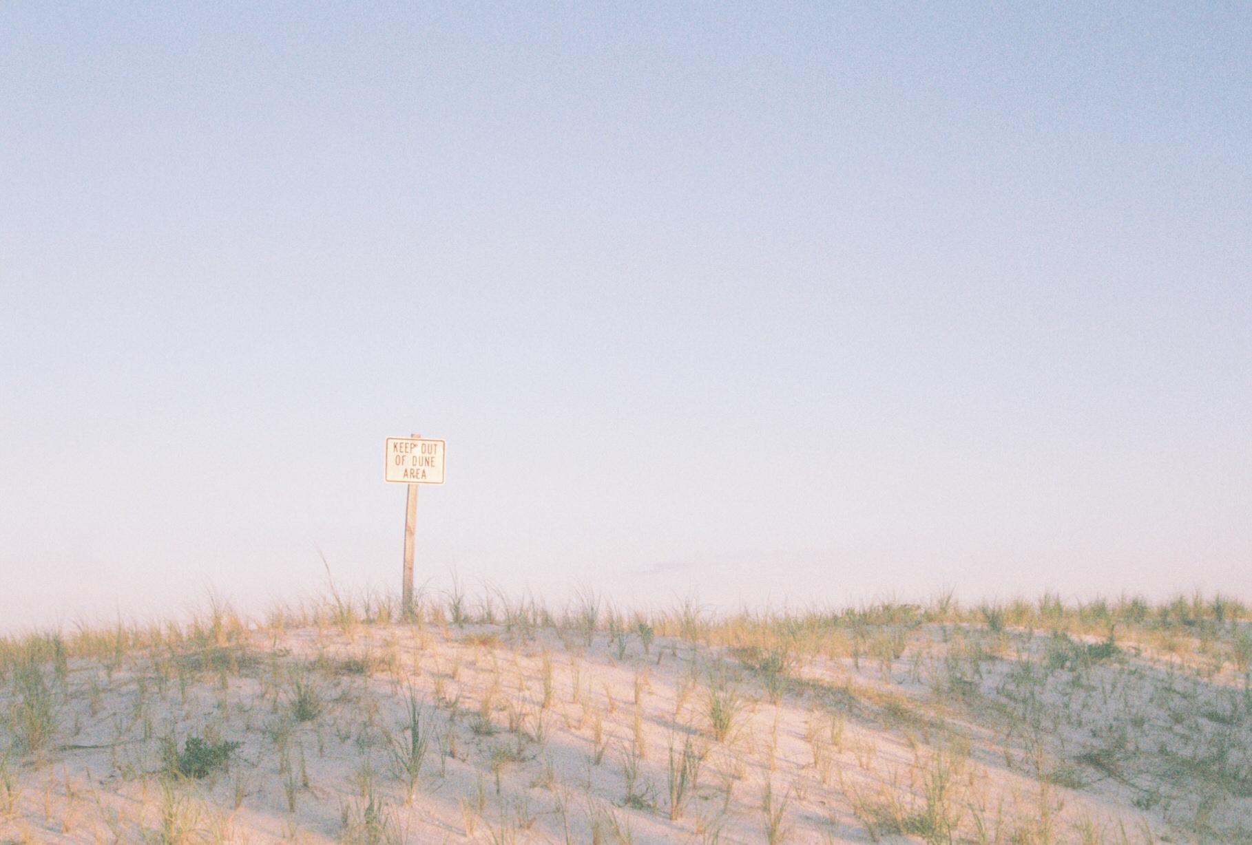 grassy sand dunes with a sign that reads 'keep out of dune area'