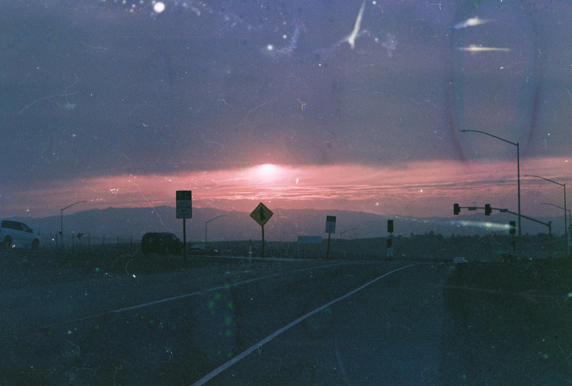 a pink sunset with a road and road signs in the foreground