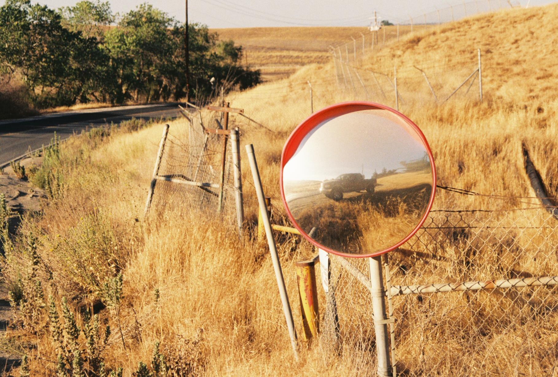 a mirror in front of dead brush, reflecting a truck