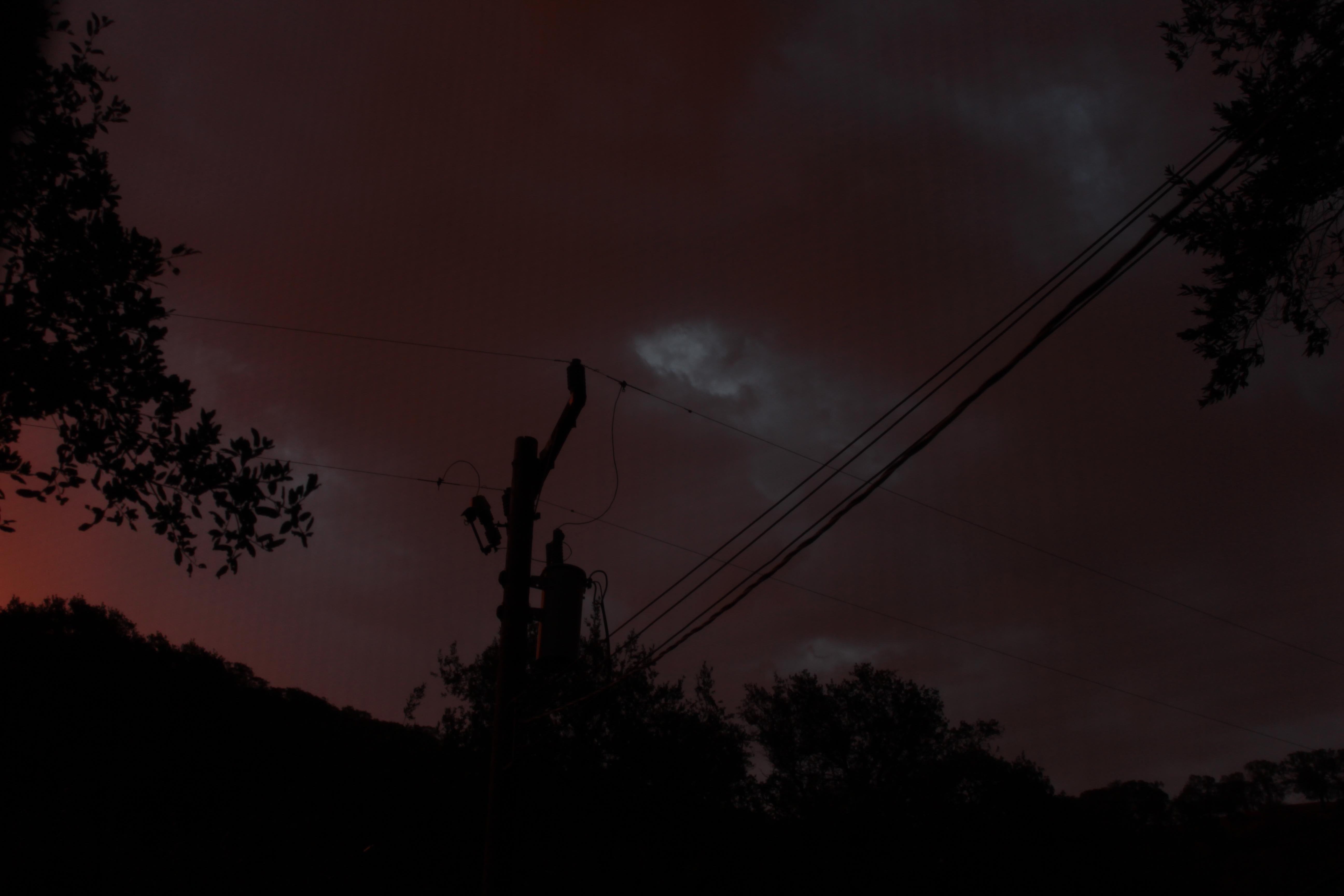 a dark pink sky filled with clouds behind shadowed hills and a telephone pole