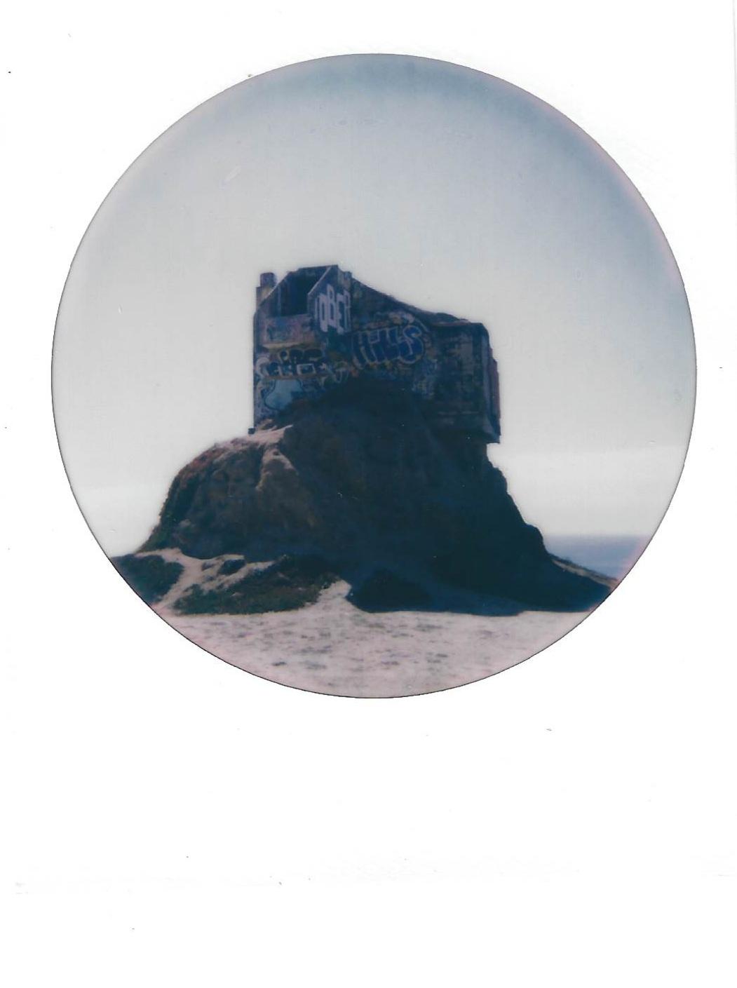 an abandoned and disheveled cement structure on top of a large rock on the beach
